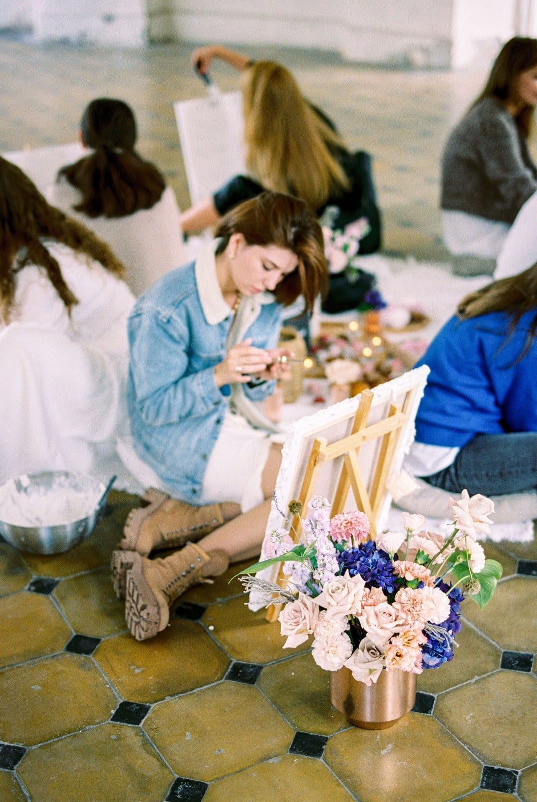 Grupo reunido a pintar em conjunto, com flores e materiais espalhados pelo chão