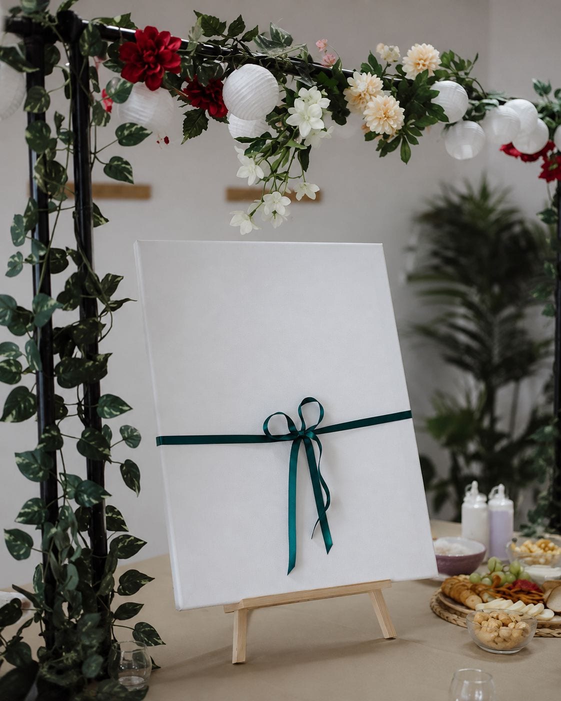 Tela em branco atada com fita verde sobre um cavalete, debaixo do arco de flores do atelier